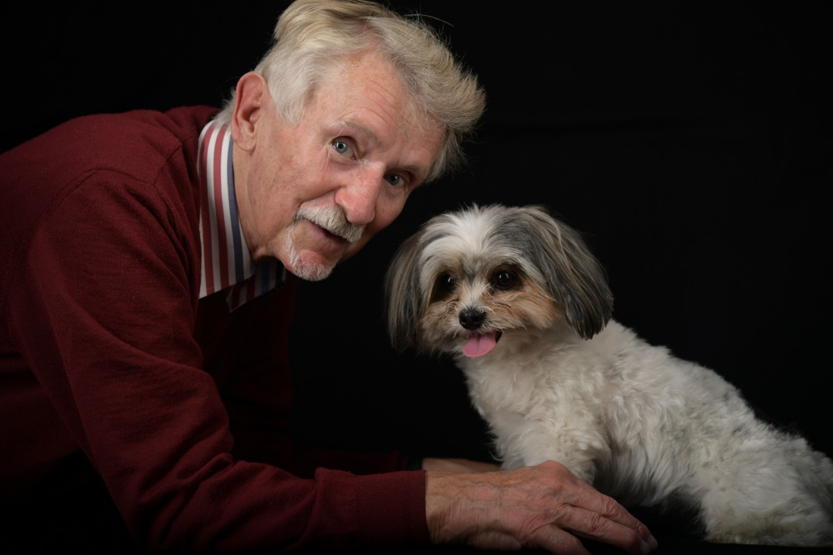 Älterer Mann mit seinem Hund im Studio, warmes Licht auf dunklem Hintergrund — Tierfotografie Berlin